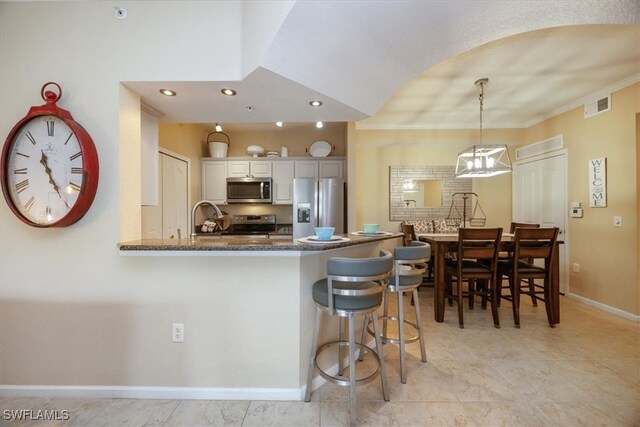 12970 Positano Cir Unit 301, Naples, FL 34105 - kitchen with appliances with stainless steel finishes, dark stone counters, white cabinets, a kitchen breakfast bar, and a peninsula
