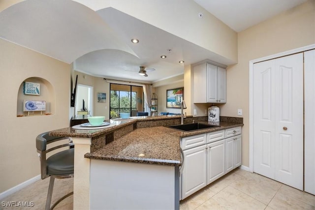 12970 Positano Cir Unit 301, Naples, FL 34105 - kitchen featuring a peninsula, dark stone countertops, a ceiling fan, a kitchen bar, and light tile patterned floors