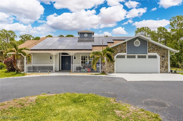 6011 Sea Grass Ln, Naples, FL 34116 - view of front facade with covered porch, stone siding, solar panels, driveway, and an attached garage
