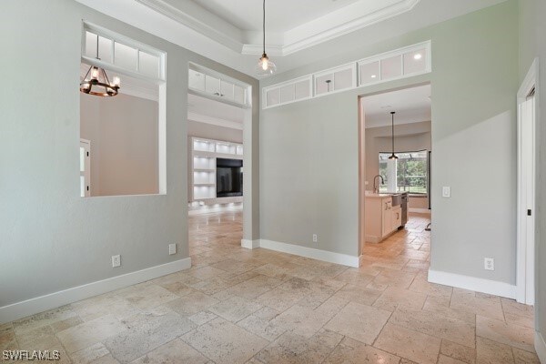 4740 5th Ave SW, Naples, FL 34119 - empty room with stone tile floors, a tray ceiling, a chandelier, and crown molding