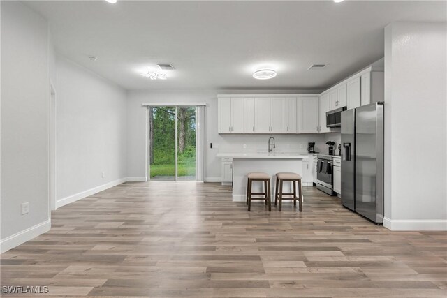 311 Long Ave S, Lehigh Acres, FL 33974 - kitchen with stainless steel appliances, light countertops, white cabinetry, light wood-style flooring, and a breakfast bar