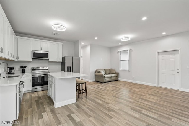 311 Long Ave S, Lehigh Acres, FL 33974 - kitchen featuring appliances with stainless steel finishes, open floor plan, a kitchen bar, light countertops, and light wood-type flooring