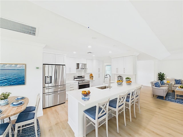 490 25th St SW, Naples, FL 34117 - kitchen with appliances with stainless steel finishes, wall chimney range hood, a kitchen breakfast bar, light wood-style flooring, and white cabinetry
