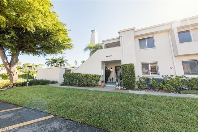 3052 Kings Lake Blvd Unit 7554, Naples, FL 34112 - view of front of house with stucco siding, a front lawn, uncovered parking, and a chimney