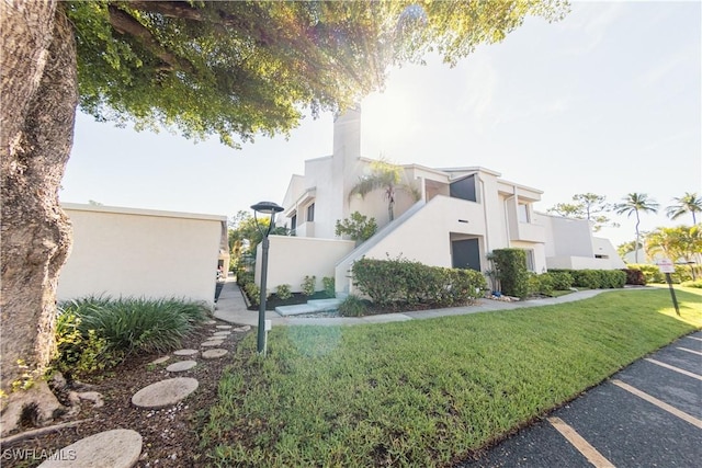 3052 Kings Lake Blvd Unit 7554, Naples, FL 34112 - view of property exterior featuring stucco siding, a lawn, uncovered parking, and a chimney
