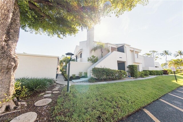 3052 Kings Lake Blvd Unit 7554, Naples, FL 34112 - view of property exterior featuring stucco siding, a lawn, uncovered parking, and a chimney