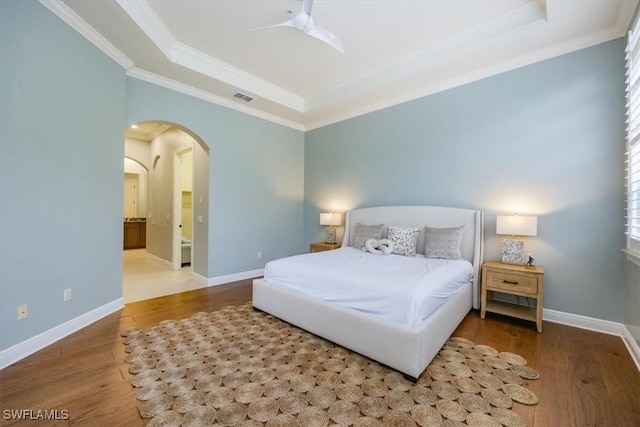 29120 Brendisi Way Unit 102, Naples, FL 34110 - bedroom featuring a tray ceiling, ornamental molding, wood finished floors, arched walkways, and ensuite bath