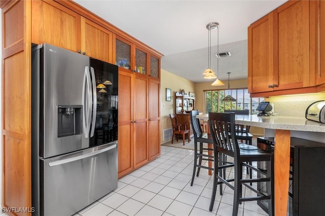 24398 Treasure Island Blvd, Punta Gorda, FL 33955 - kitchen featuring stainless steel refrigerator with ice dispenser, light tile patterned flooring, brown cabinets, and decorative light fixtures
