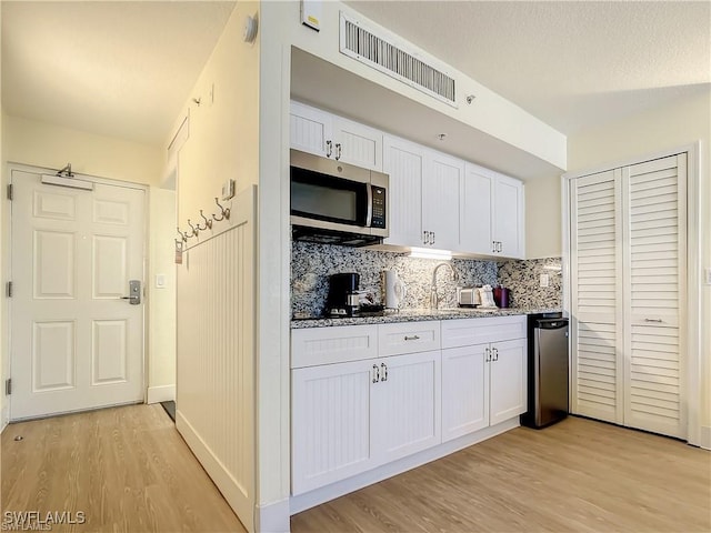 140 Estero Blvd Unit 2206, Fort Myers Beach, FL 33931 - kitchen featuring stainless steel microwave, light wood-type flooring, white cabinetry, light stone counters, and tasteful backsplash