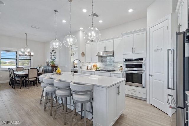 2703 Aviamar Cir, Naples, FL 34114 - kitchen with stainless steel appliances, light countertops, tasteful backsplash, a chandelier, and light wood-style flooring