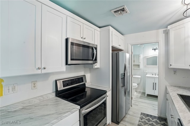 4011 Coconut Cir S, Naples, FL 34104 - kitchen featuring appliances with stainless steel finishes, white cabinets, light wood finished floors, and light stone countertops