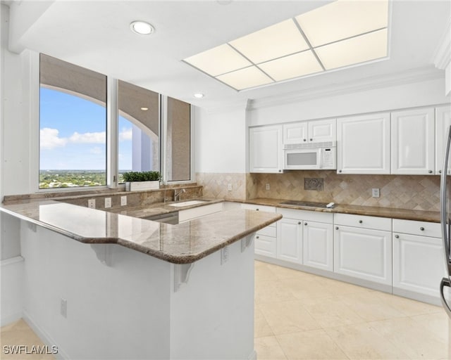 7117 Pelican Bay Blvd Unit 1903, Naples, FL 34108 - kitchen featuring white microwave, dark stone countertops, a kitchen bar, white cabinetry, and decorative backsplash