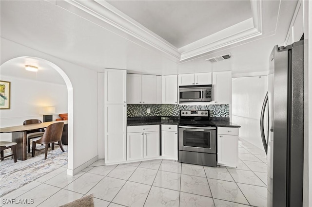 1442 Wellington Ct, Cape Coral, FL 33904 - kitchen with appliances with stainless steel finishes, dark countertops, arched walkways, white cabinetry, and tasteful backsplash
