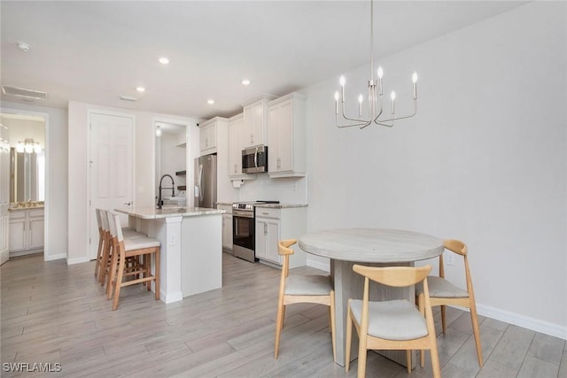 14671 Edgewater Cir, Naples, FL 34114 - kitchen with stainless steel appliances, a center island with sink, light wood-type flooring, a breakfast bar area, and white cabinets