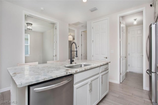 14671 Edgewater Cir, Naples, FL 34114 - kitchen featuring appliances with stainless steel finishes, white cabinetry, light wood-type flooring, light stone countertops, and a center island with sink