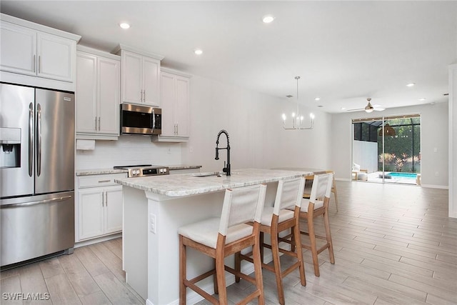 14671 Edgewater Cir, Naples, FL 34114 - kitchen with stainless steel appliances, open floor plan, light wood-style floors, tasteful backsplash, and an island with sink