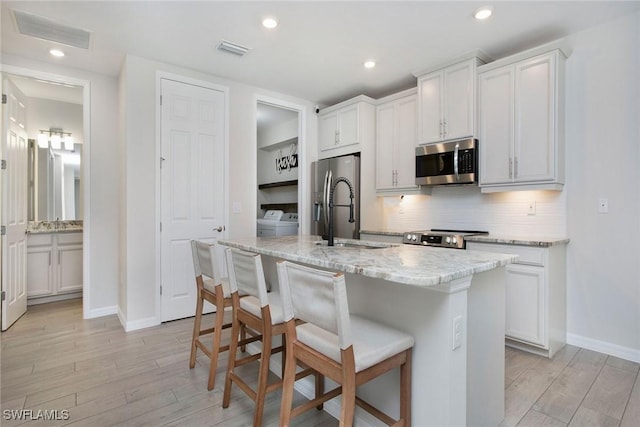 14671 Edgewater Cir, Naples, FL 34114 - kitchen featuring appliances with stainless steel finishes, light wood finished floors, a kitchen bar, a center island with sink, and decorative backsplash