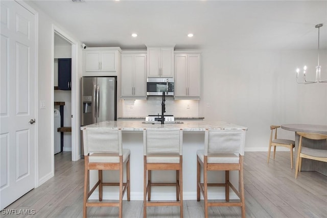 14671 Edgewater Cir, Naples, FL 34114 - kitchen featuring stainless steel appliances, light wood finished floors, backsplash, a kitchen island with sink, and a kitchen bar
