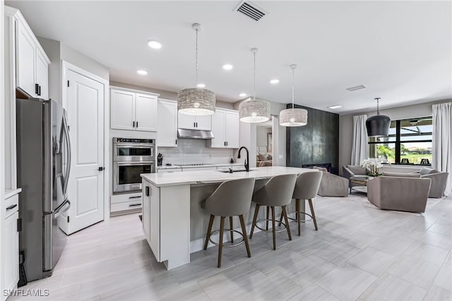 19604 Beechcrest Pl, Estero, FL 33928 - kitchen with stainless steel appliances, under cabinet range hood, open floor plan, a kitchen bar, and white cabinets