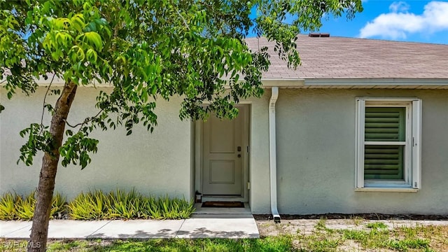 9059 Aegean Cir, Lehigh Acres, FL 33936 - view of exterior entry featuring stucco siding and roof with shingles