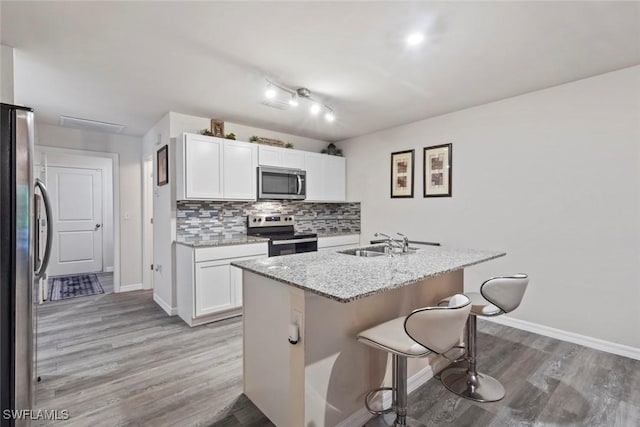 9059 Aegean Cir, Lehigh Acres, FL 33936 - kitchen with appliances with stainless steel finishes, a kitchen breakfast bar, white cabinets, backsplash, and light wood-style floors