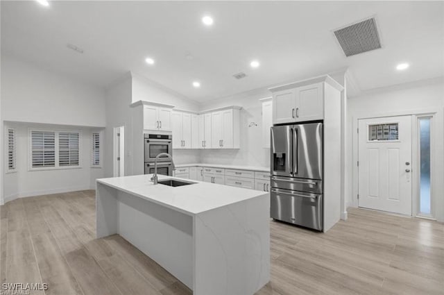 16131 Kelly Woods Dr, Fort Myers, FL 33908 - kitchen featuring stainless steel appliances, lofted ceiling, an island with sink, white cabinetry, and light wood finished floors