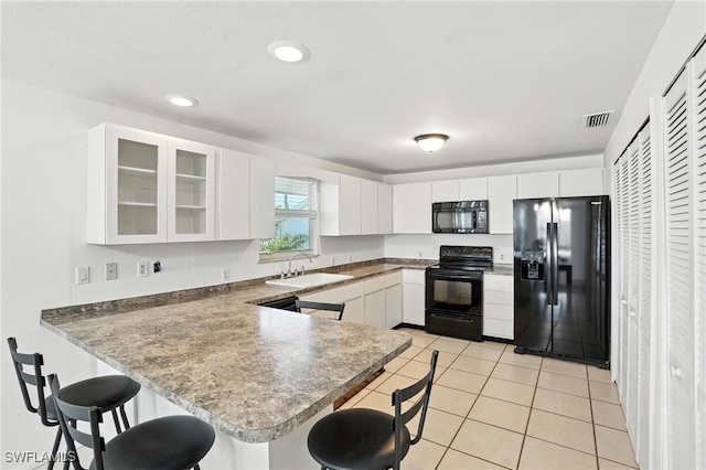 131 Bay Mar Dr, Fort Myers Beach, FL 33931 - kitchen featuring black appliances, a kitchen bar, a peninsula, glass insert cabinets, and white cabinets