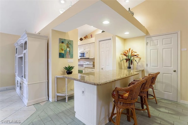 796 108th Ave N, Naples, FL 34108 - kitchen with white appliances, a breakfast bar, light stone counters, a peninsula, and recessed lighting