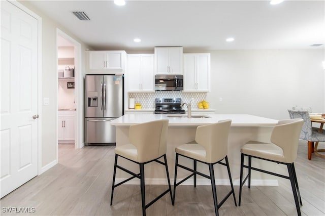 14727 Edgewater Cir, Naples, FL 34114 - kitchen featuring appliances with stainless steel finishes, light countertops, backsplash, a kitchen bar, and white cabinetry