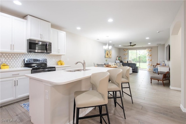 14727 Edgewater Cir, Naples, FL 34114 - kitchen with electric range oven, stainless steel microwave, open floor plan, a center island with sink, and light wood finished floors