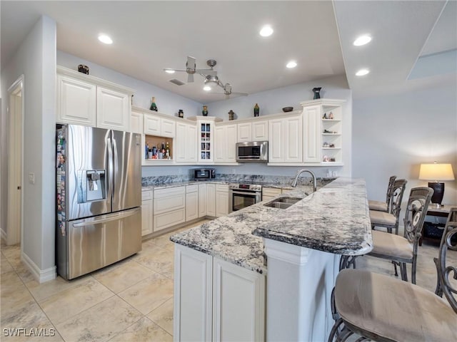 2705 SW 30th Ter, Cape Coral, FL 33914 - kitchen featuring stainless steel appliances, open shelves, a peninsula, a kitchen bar, and light stone counters