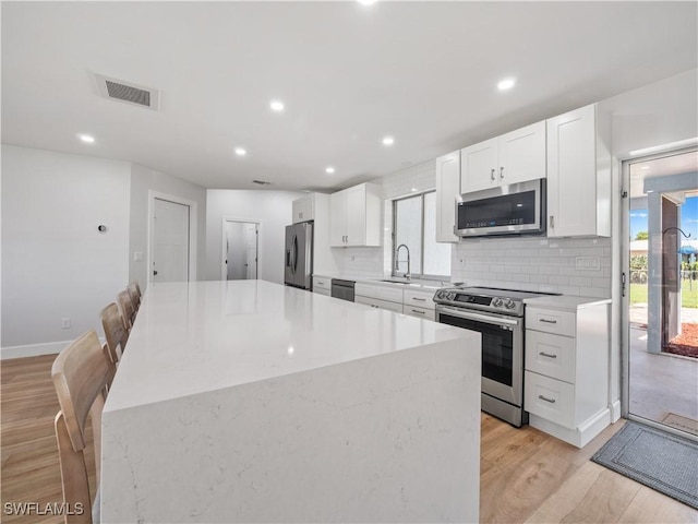 505 Monterey Ave, Cape Coral, FL 33904 - kitchen with appliances with stainless steel finishes, white cabinetry, decorative backsplash, a center island, and light wood-style flooring