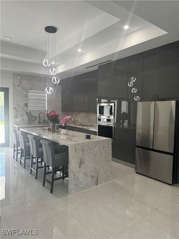 4067 33rd Ave NE, Naples, FL 34120 - kitchen featuring stainless steel appliances, a tray ceiling, decorative light fixtures, light stone counters, and a large island