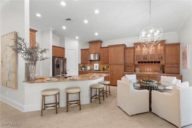 8888 Savona Ct, Naples, FL 34119 - kitchen with under cabinet range hood, stainless steel fridge with ice dispenser, a peninsula, ornamental molding, and a kitchen breakfast bar
