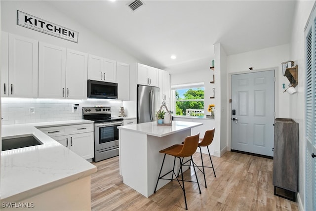 162 Pebble Shores Dr Unit 203, Naples, FL 34110 - kitchen featuring appliances with stainless steel finishes, backsplash, white cabinetry, a kitchen bar, and light wood-style flooring
