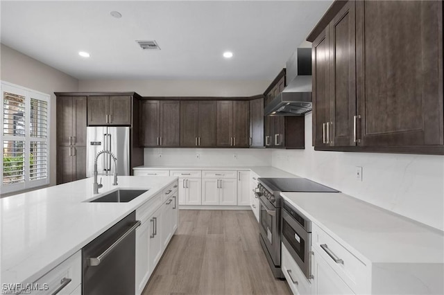 16409 Coco Hammock Way, Fort Myers, FL 34135 - kitchen with appliances with stainless steel finishes, wall chimney range hood, dark brown cabinetry, light countertops, and light wood-type flooring