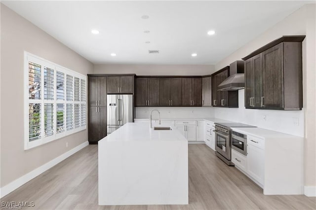 16409 Coco Hammock Way, Fort Myers, FL 34135 - kitchen featuring high quality appliances, wall chimney range hood, dark brown cabinetry, light countertops, and light wood-style floors