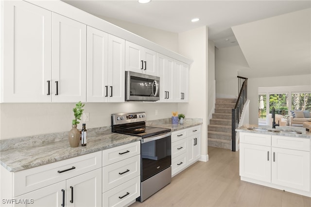 211 11th St NW, Naples, FL 34120 - kitchen with stainless steel appliances, white cabinets, light wood-type flooring, light stone counters, and recessed lighting