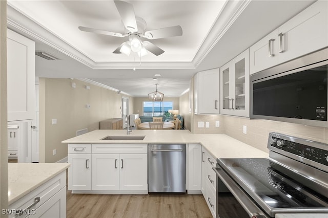 3067 W Gulf Dr Unit 102, Sanibel, FL 33957 - kitchen featuring stainless steel appliances, a tray ceiling, a peninsula, ornamental molding, and tasteful backsplash