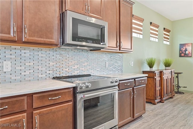 3344 Apple Blossom Dr, Alva, FL 33920 - kitchen featuring stainless steel appliances, light wood-style flooring, tasteful backsplash, brown cabinets, and light stone countertops