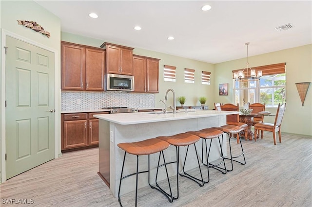 3344 Apple Blossom Dr, Alva, FL 33920 - kitchen with stainless steel microwave, a kitchen bar, a chandelier, light wood-type flooring, and brown cabinetry