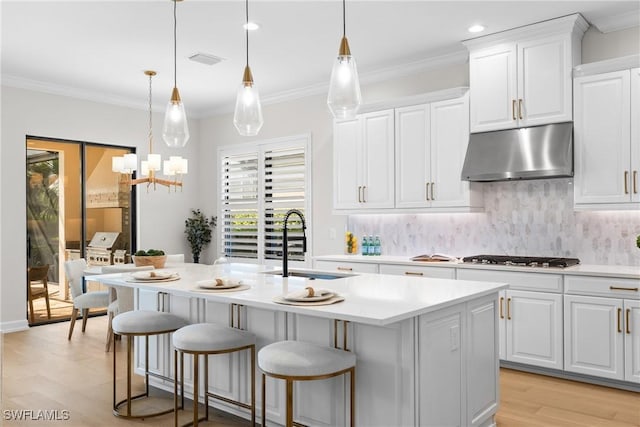 8834 Vaccaro Ct, Naples, FL 34119 - kitchen featuring under cabinet range hood, gas stovetop, light countertops, light wood finished floors, and a chandelier