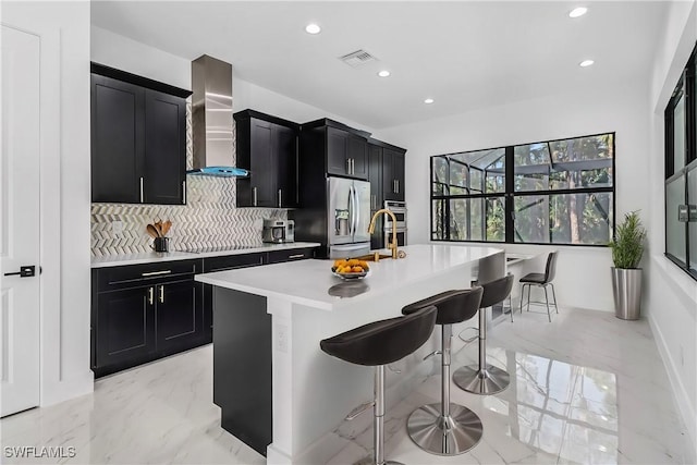 491 9th St SW, Naples, FL 34117 - kitchen with dark cabinets, wall chimney exhaust hood, appliances with stainless steel finishes, decorative backsplash, and light countertops