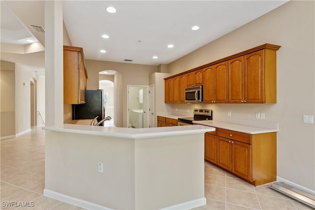 26425 Lucky Stone Rd Unit 201, Bonita Springs, FL 34135 - kitchen featuring appliances with stainless steel finishes, arched walkways, light tile patterned flooring, brown cabinets, and a peninsula