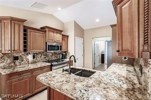 4238 Golfair Ln, North Port, FL 34288 - kitchen featuring stainless steel appliances, decorative backsplash, light stone counters, vaulted ceiling, and a peninsula