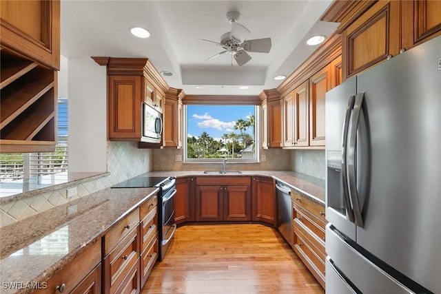420 Cove Tower Dr Unit 304, Naples, FL 34110 - kitchen with stainless steel appliances, brown cabinetry, light stone counters, ceiling fan, and light wood-style floors