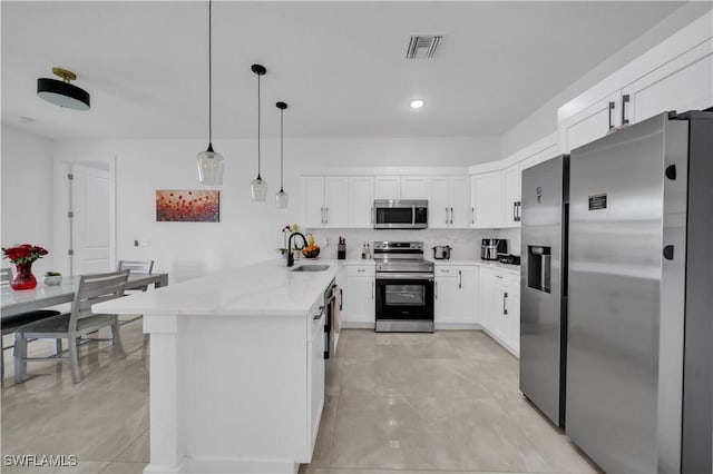 2607 4th St SW, Lehigh Acres, FL 33976 - kitchen featuring stainless steel appliances, a peninsula, white cabinets, hanging light fixtures, and light stone countertops