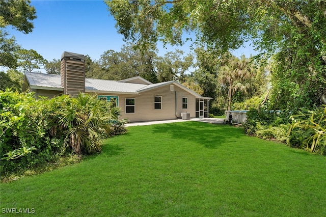 19350 Meredith Rd, North Fort Myers, FL 33917 - rear view of house featuring a chimney, a patio, a yard, a metal roof, and view of scattered trees