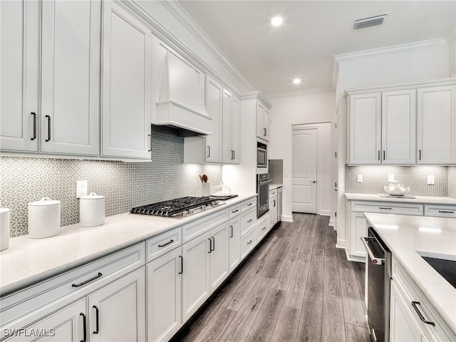 6992 Chapel Creek Ln, North Fort Myers, FL 33917 - kitchen with appliances with stainless steel finishes, premium range hood, white cabinets, ornamental molding, and backsplash