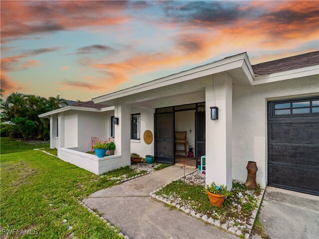 17577 Moorfield Dr, Fort Myers, FL 33908 - exterior entry at dusk featuring stucco siding, a lawn, and a garage